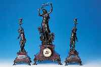 Kaminuhr mit zwei Beistellern, Frankreich, um 1910, dunkelrot geäderter Marmorsockel, bro-nzierte Metallappliken, Figurenbekrönung mit Putten, ...