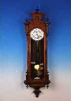 WANDUHR, GUSTAV BECKER, UM 1892, VERZIERTES U. FURNIERT. HOLZGEHäUSE, ORIGINALAUFSATZ, DREISEITIG VERGLAST, ZWEIGETEILT. EMAILZIFFER-BLATT MIT ...