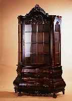 GLASVITRINE, HOLLAND, UM 1930, WURZELNUSS- FURNIERT, Z. T. GESPIEGELT, MAHAGONI GEBEIZT, DREISEITIG VERGLAST, GESCHNITZTE APPLIKA- TIONEN, DREI ...