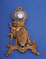 UHRENSTäNDER DARSTELLUNG AMOR, PANTOFFEL HAL- TEND UMGEB. M. ÖSE RüCKS. ALS WANDANH., MES-SING VERG., BER., UM 1890, H. CA. 22 CM, ...