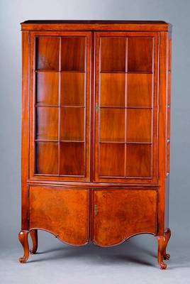 Vitrine, deutsch, um 1925, Nußbaum/ Wurzelnuß, Unterteil geschweift, 2-türig, Füße in Voluten auslaufend, Oberteil 3-seitig verglast ...