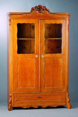 Vitrinenschrank, Louis-Philippe, um 1860, Kirschbaumfurnier, sog. Brezelfüllungen, teilverglast, Teile erneuert, Kopf m. Volutenschnitzerei, ...