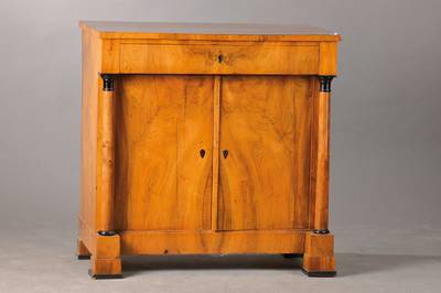 Biedermeierhalbschrank, wohl Mainz um 1810, Nussbaum gespiegelt furniert z.T. massiv, 2-türig, seitl. Vollsäulen stützen denÜberbauschub, ...