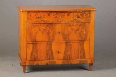 Kommode, wohl süddeutsch um 1830, Nussbau m- bzw. Wurzelnussfurnier z.T. doppelt gespiegelt auf Weichholzkorpus verlegt, 3-schübig, oberer Schub ...