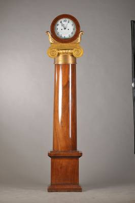 Standuhr, Lüneburg um 1820, Nußbaum poliert,Sockel in Plinthenform, daruf halbrunde Säule als Türe in Demi-Lune, darüber ionisches Kapitell mit ...