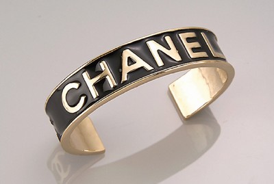 CHANEL Armreif, Metall verg., schlichtes Design, Schriftzug und Logo erhaben gearbeitetHintergrund mit schwarzem Hartlack, D. ca. 5.7cm, B. ca. 1.5 ...