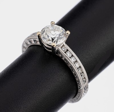 18 kt Gold Brillant-Ring, WG 750/000, mittig erhaben gefasster Brillant ca. 1.01 ct (grav.) Weiß/si, Ringschultern mit 14 Brillanten zus. ca. 0.23 ...
