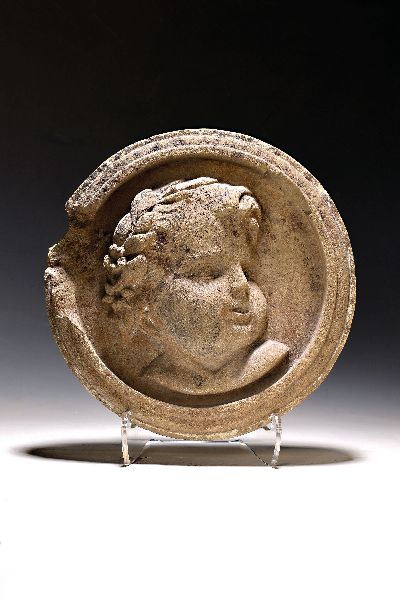 Wandapplike, deutsch, 18. Jh., heller Sandstein, mittig Relief eines Bacchantenkopfes, Umrandung besch., H. ca. 6cm, D. ca. 35cm