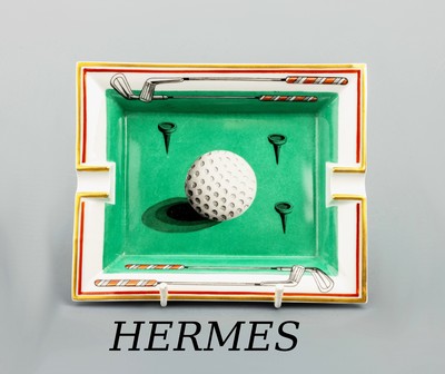 HERMES Aschenbecher, "Golfball", weißes Porzellan, goldfarb./roter Rand, grüner Boden,Golfball und Golfschläger, ca. 20 x 16 cm
