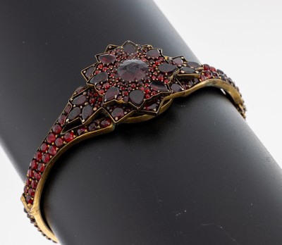 Granat-Armreif, Böhmen um 1880-1900, Metallverg., Oberteil in mehreren Ebenen, Spiegelgranate und rundfacett. Granate, ca. 5.8 x 5.2 cm, ...
