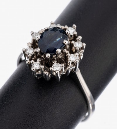 14 kt Gold Saphir-Brillant-Ring, WG 585/000, mittig erhaben gefasster ovalfacett. Saphir ca. 1.0 ct, umgeben von 8 Brillanten zus. ca. 0.16 ct ...