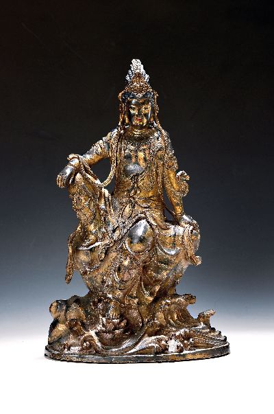 Große Guanyin/Guan Yin, China, wohl um 1900, Bronze, auf erhöhtem Felsvorsprung sitzende Gottheit, ein Fuß auf einer Lotusblüte platziert, das ...