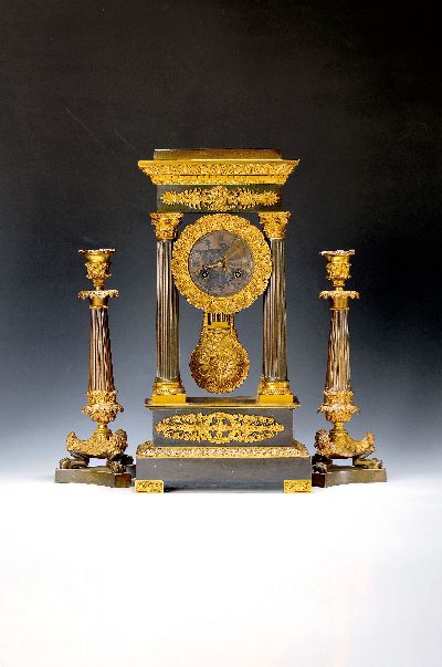 Portaluhr und zwei Kerzenbeistellern, Frankreich, um 1870, Bronze z.T. patiniert, aufwendig mit Blattdekor und Applikationen, kannelierte Säulen mit ...