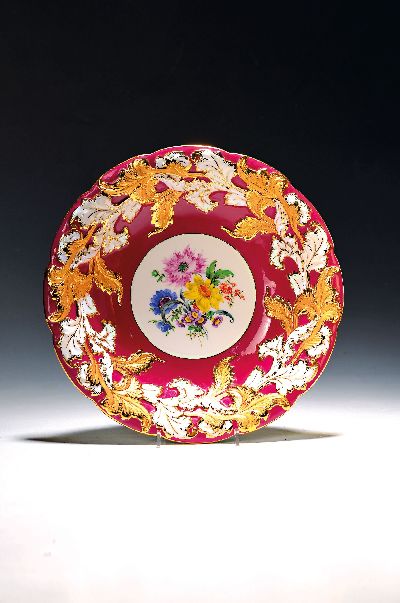 Prunkschale, Meissen, 1970er Jahre, 1. Wahl,reliefiert, matt- und glanzvergoldet, partiell weinrot glasiert, mittig bunte Blumenmalerei, D. ca. 30.5cm