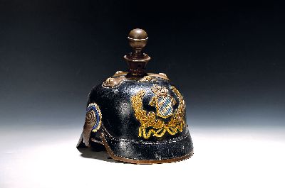 Feuerwehrhelm aus Bayern, um 1900, Lederkorpus, Messingapplikation mit bemaltem Rautenschild (berieben), beide Kokarden, gewölbte Schuppenketten, ...