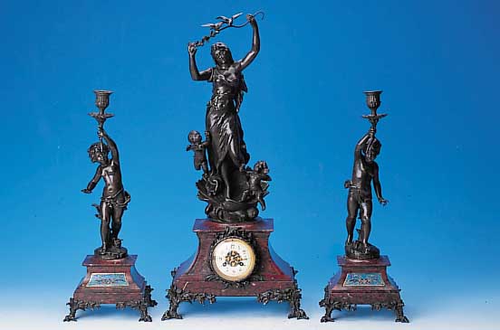 Kaminuhr mit zwei Beistellern, Frankreich, um 1910, dunkelrot geäderter Marmorsockel, bro-nzierte Metallappliken, Figurenbekrönung mit Putten, ...