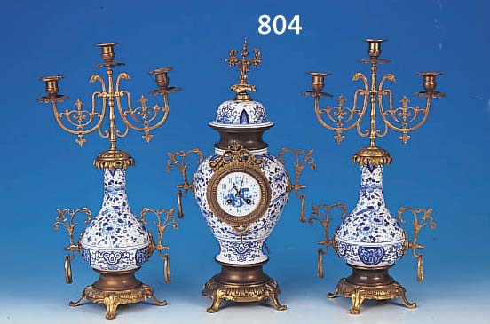 VASENUHR MIT ZWEI BEISTELLERN, WOHL FLANDERN, UM 1920/30, KERAMIK MIT BLAUER CAMAIEU-MA- LEREI, MESSINGMONTUREN, GLASDECKEL, EMAILZIF- FERBLATT MIT ...