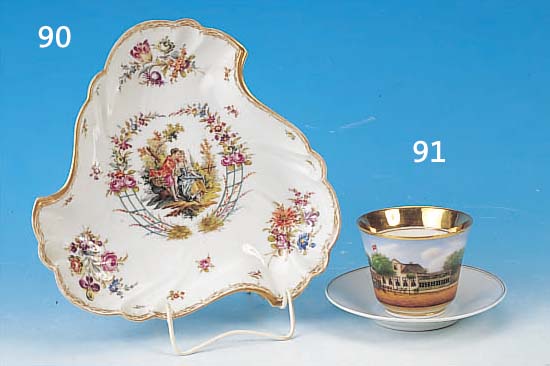 ZIERTASSE MIT UNTERTASSE, THüRINGEN, UM 1890, PORZELLAN, GROßE KARTUSCHE MIT ANSICHT EINER FARM, VERMUTL. IN DEUTSCH-SüDWEST-AFRI- KA, FEINE ...