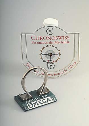 KONVOLUT BESTEHEND AUS EINEM TASCHENUHRSTäNDERVON OMEGA UND EINEM CHRONOSWISS WERBESCHILD, STäNDER ZUM TEIL EMAILL., Z.T. LT. BEST., ANBEI ...