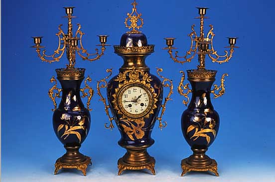 KAMINUHR MIT ZWEI BEISTELLERN, FRANKREICH/ BELGIEN, UM 1900-1920, KOBALTBLAUES KERAMIK-GEHäUSE, MESSINGAPPLIKEN, ZWEI FüNFFLAMMIGE ...