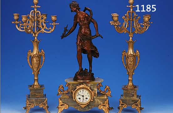 KAMINUHR MIT ZWEI BEISTELLERN, FRANKREICH, UM 1900, ONYXSOCKEL MIT VERZIERTEN SPRITZ- GUßFüßEN, FIGURENBEKRöNUNG SIGN. AUG. MOREAU, ...