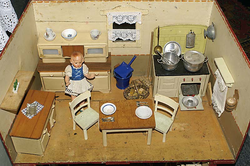 PuppenkÜche, 30/40er J., mit PÜppchen, schÖn eingerichtet mit Tisch und StÜhlen, Anrichte, Kommode und Ofen, ca. 31x60x34cm, l. bespielt