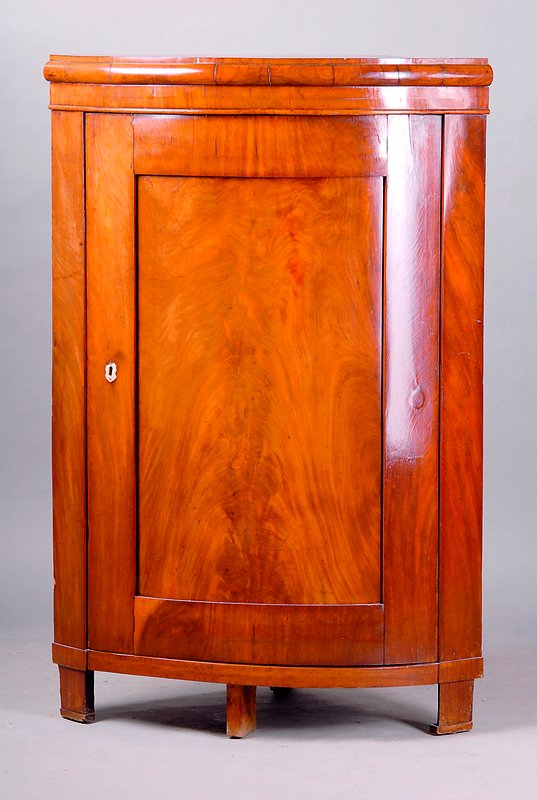 Eckschrank, norddeutsch, um 1860, Nußbaum auf Mahagoni gebeizt, Front gebogt, Inlet getreppt, einfacher Wulst, Beinbeschl., dieser teilw. besch., ...