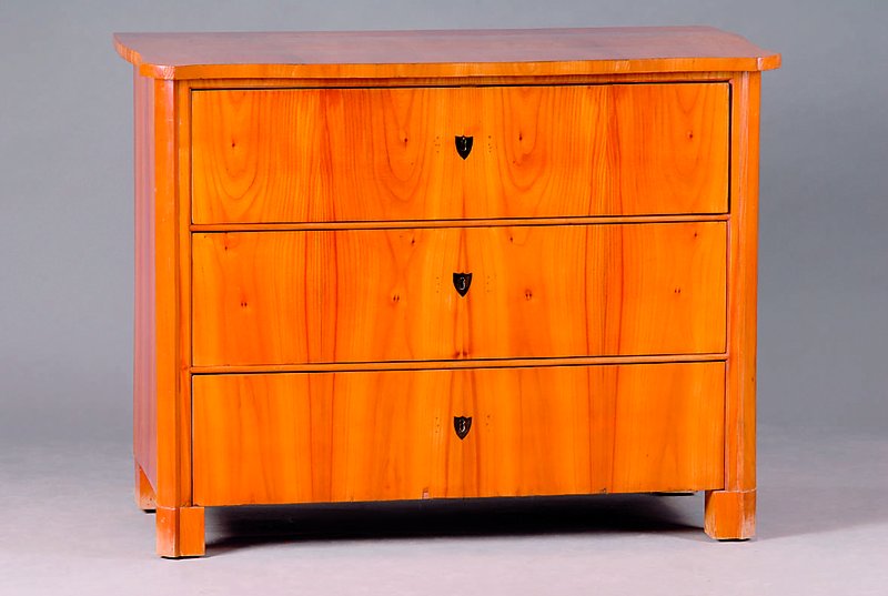 Kommode, Biedermeier, um 1835, Kirschbaum, 3-schübig, orig. Beschl., Ecken abgeflacht, schwundrissig, Platte fleckig, st. Gebr.-Sp., SP. 1200,-, ca. ...