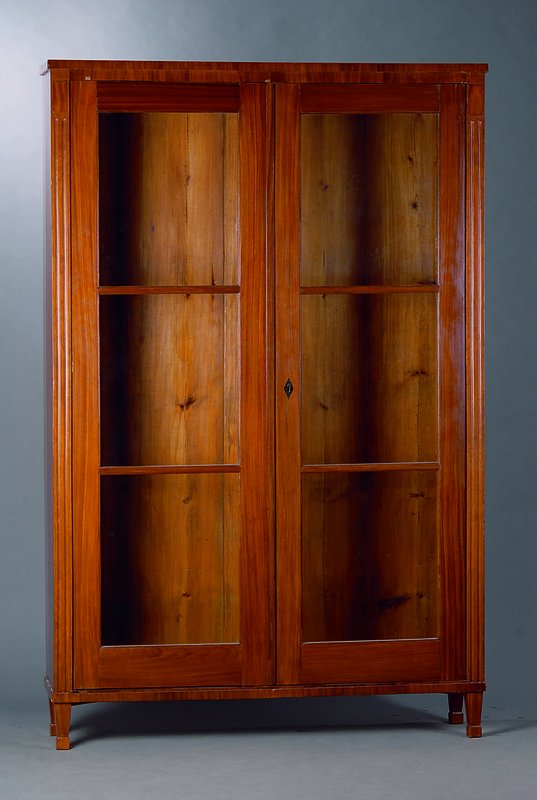 Bücherschrank, Berlin, um 1830/40, Mahagoni, im Schinkelstil, 2-türig, verglast und versprosst, Lisenen gerieft, Furnierteile fehlen, Füße sek., ...