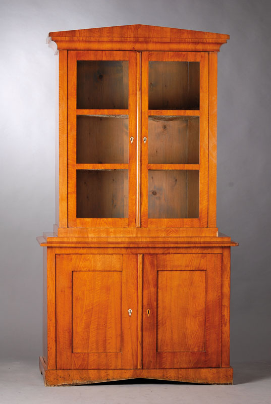 Aufsatzschrank, wohl Berlin um 1815, Kirschbaum massiv, Kopf mit spitz zulaufendem Kapitel, 3-fach getreppt mit Hohlkehle, Vitrinenteil 2-türig mit ...