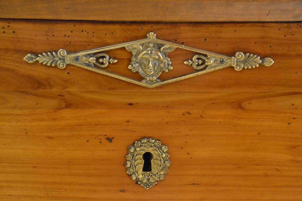 Detail a: Säulenkommode, Empire um 1800, Kirschbaum massiv, seitl. Halbsäulen, Seiten je kassettiert, 3-schübig, reicher Messingbeschlag, rest., Reste alten ...