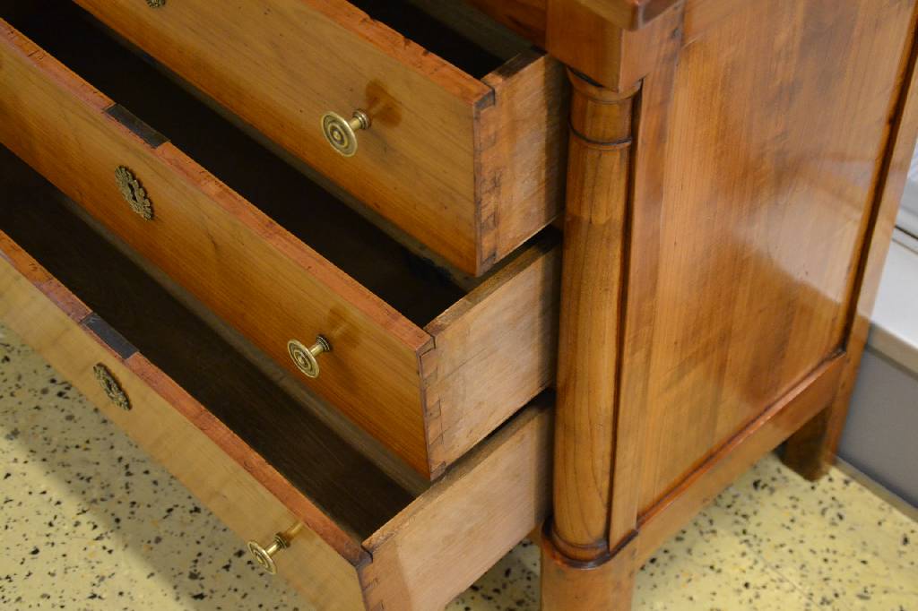 Detail b: Säulenkommode, Empire um 1800, Kirschbaum massiv, seitl. Halbsäulen, Seiten je kassettiert, 3-schübig, reicher Messingbeschlag, rest., Reste alten ...