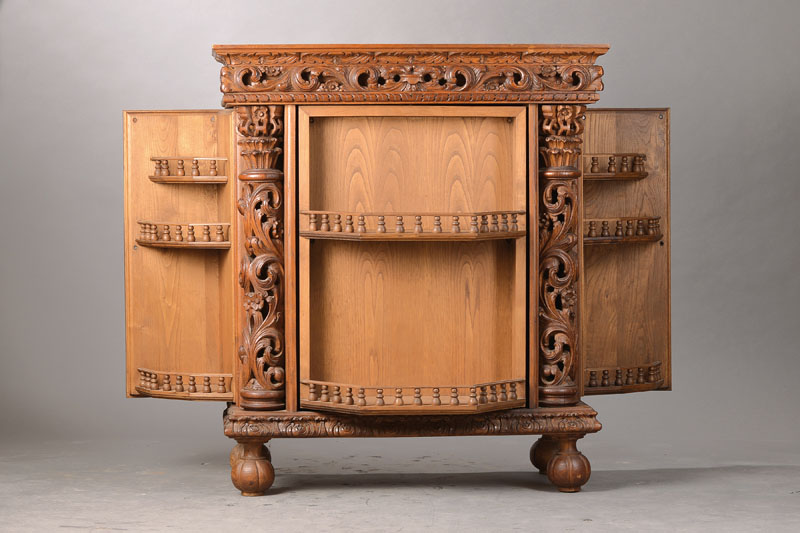 Detail a: Barschrank, deutsch um 1955/60, Eiche z.T. massiv, reiche Figuren- u. Akanthusblattschnitzerei z.T. aus dem Vollholz, drehbare TÜr mit rückseitiger ...