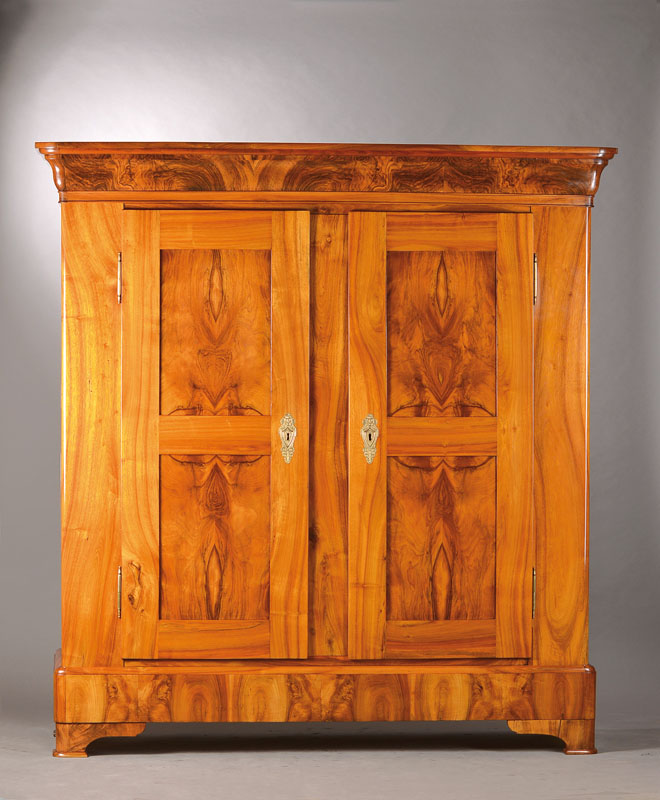 Biedermeierschrank, wohl Bodensee um 1820/30, Nussbaum massiv bzw. Wurzelnuss doppelt gespiegelt furniert, ausladendes Gesims u. Wangen, Türen u. ...
