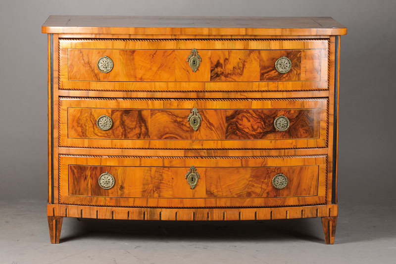 Barockkommode, wohl Gegend Karlsruhe, um 1800, Nussbaum- bzw. Wurzelnussfurnier z.T. auf Kreuzfuge auf Weichholzkorpus verlegt, 3- schübig, Band-, ...
