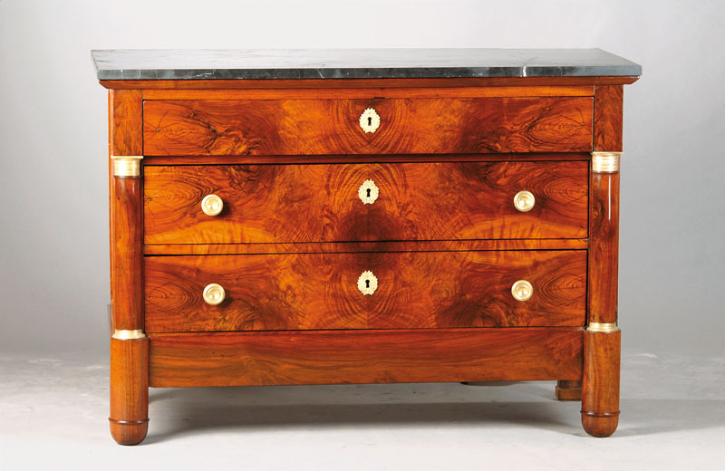 Empire-Kommode, 19.Jh., Nussbaum furniert auf Weichholzkorpus, 3-schübig, Messing-Appliken, seitlich Halbsäulen, schwarze Marmorplatte, ca. ...