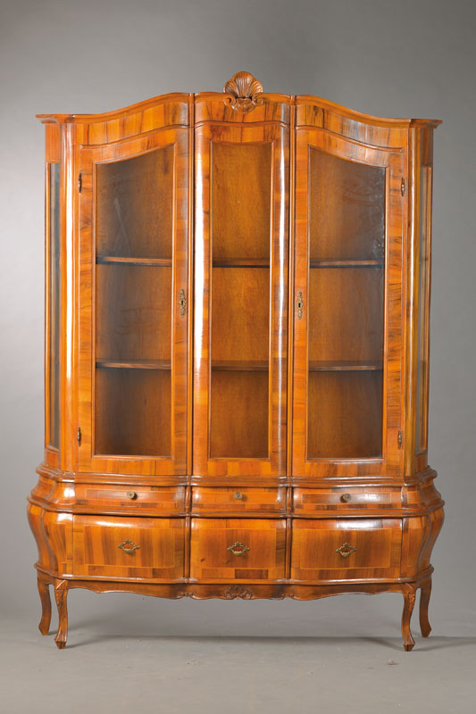 Aufsatzvitrine im Barockstil, Frühes 20.Jh., Nussbaumfurnier auf Buchekorpus, 3-türig, 3- seitig verglast, bombierter Unterbau mit 6 Schubladen u. ...