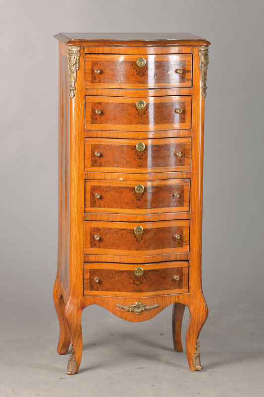 Kleiner Schubladenschrank, sog. Chiffonieré bzw. Pfeilerkommode, 70er Jahre, Nussbaum- bzw. Wurzelnussfurnier, Front geschweift, Messingappliken, ...