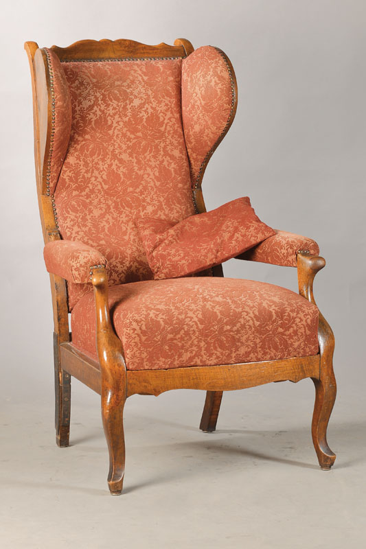 Ohrenbackensessel, südwestdeutsch, wohl Mainz, um 1820/30, Nussbaum massiv u. furniert, allseitig geschweifte Form, in sich gewölbte Rückenlehne, ...