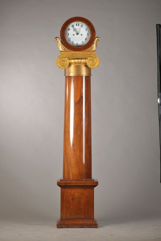 Standuhr, Lüneburg um 1820, Nußbaum poliert,Sockel in Plinthenform, daruf halbrunde Säule als Türe in Demi-Lune, darüber ionisches Kapitell mit ...