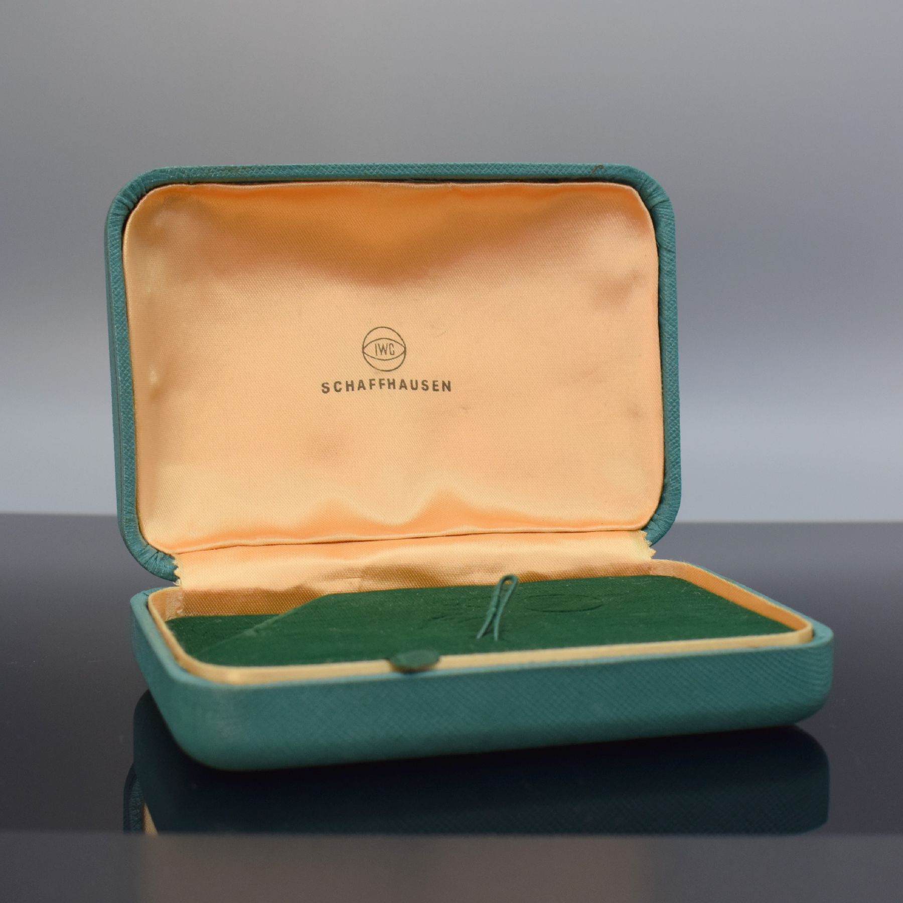 Detail a: IWC seltene Armbanduhr-Box, Schweiz um 1960, Aussen m. Stoff bezogen, gefederter Deckel, innen grüner Samt bzw. goldfarb. Stoff mit IWC Symbolik, ...
