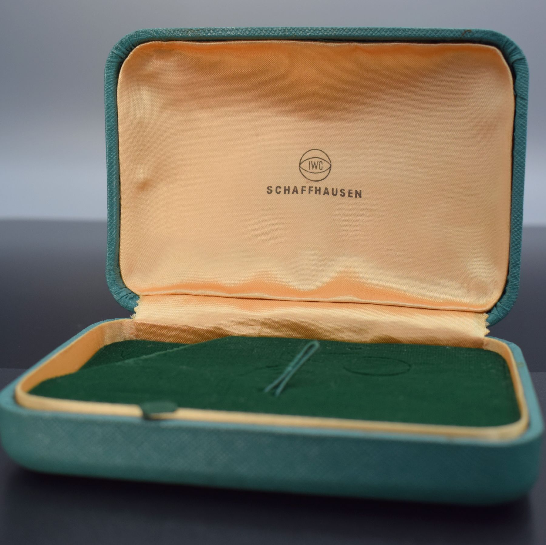 Detail b: IWC seltene Armbanduhr-Box, Schweiz um 1960, Aussen m. Stoff bezogen, gefederter Deckel, innen grüner Samt bzw. goldfarb. Stoff mit IWC Symbolik, ...