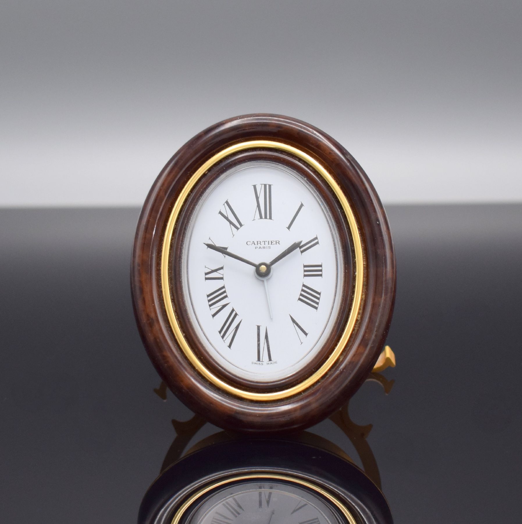 CARTIER Paris Tischwecker, Schweiz 1980er Jahre, quarz, Ref. 7519, verg. Messinggeh. z. T. in Holzoptik braun lackiert, emailfarb. Zifferbl. m. röm. ...