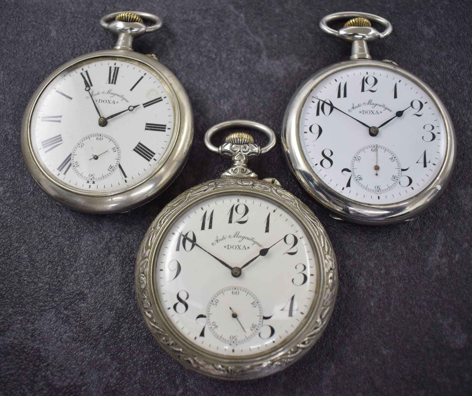 3 DOXA große offene Taschenuhren, Schweiz um 1900, Kronenaufzug, Nickelgehäuse, Emailzifferbl. teils besch. m. arab. Zahlen, Stahlzeiger, ...