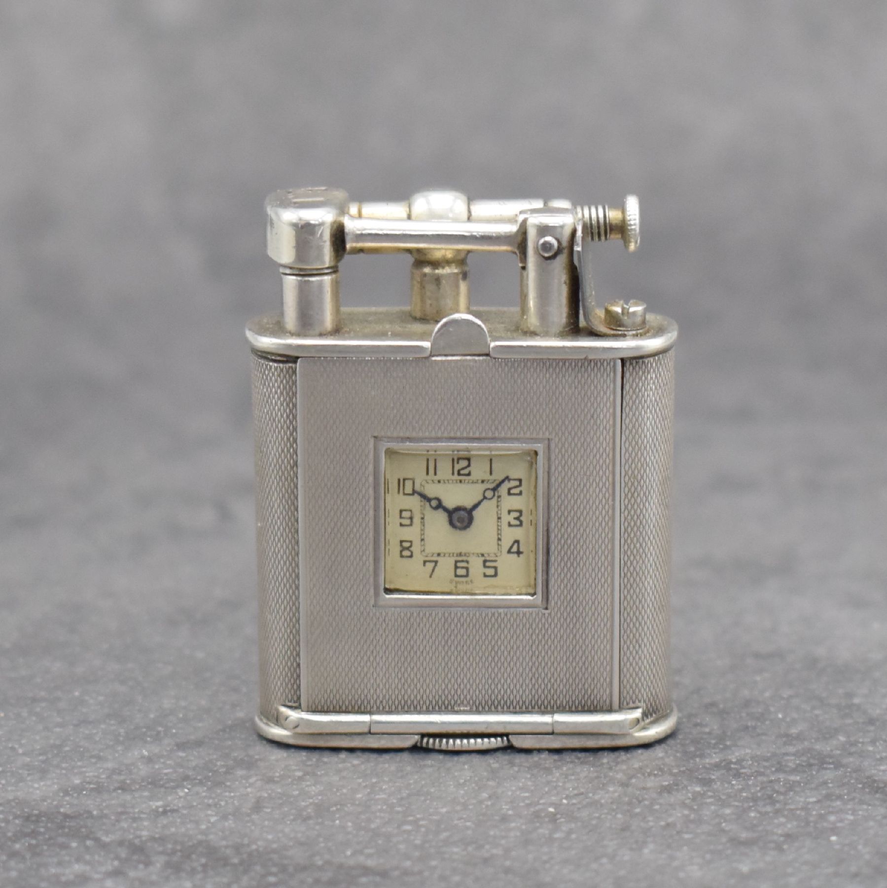 Benzinfeuerzeug mit eingelassener Uhr in 900er Silber, Schweiz um 1930, rundum guill. Geh., Front mit Scharnier aufklappbar, Boden über verg. Werk ...