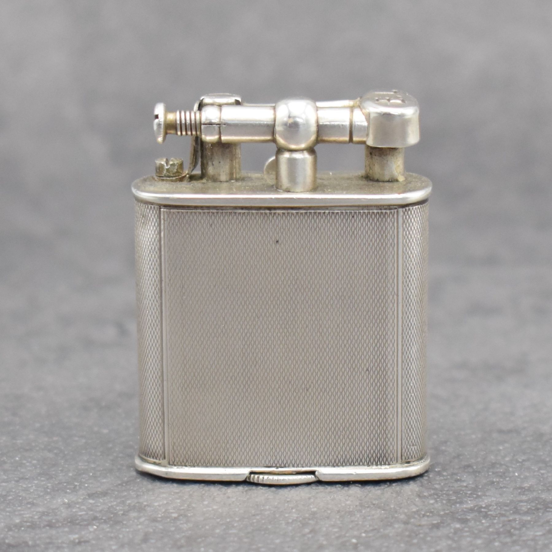 Detail b: Benzinfeuerzeug mit eingelassener Uhr in 900er Silber, Schweiz um 1930, rundum guill. Geh., Front mit Scharnier aufklappbar, Boden über verg. Werk ...
