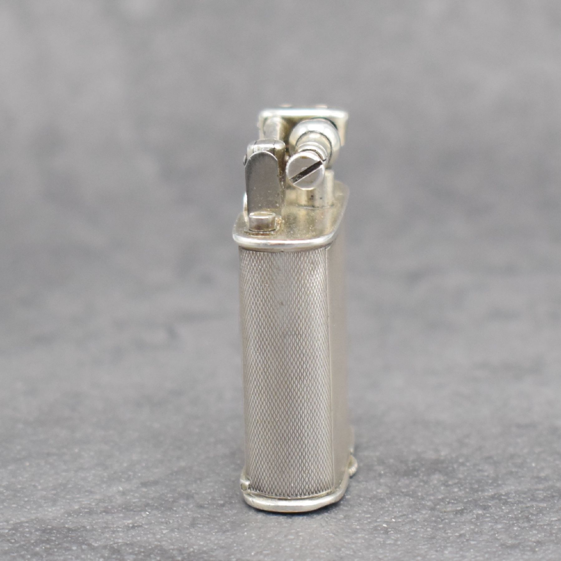 Detail c: Benzinfeuerzeug mit eingelassener Uhr in 900er Silber, Schweiz um 1930, rundum guill. Geh., Front mit Scharnier aufklappbar, Boden über verg. Werk ...