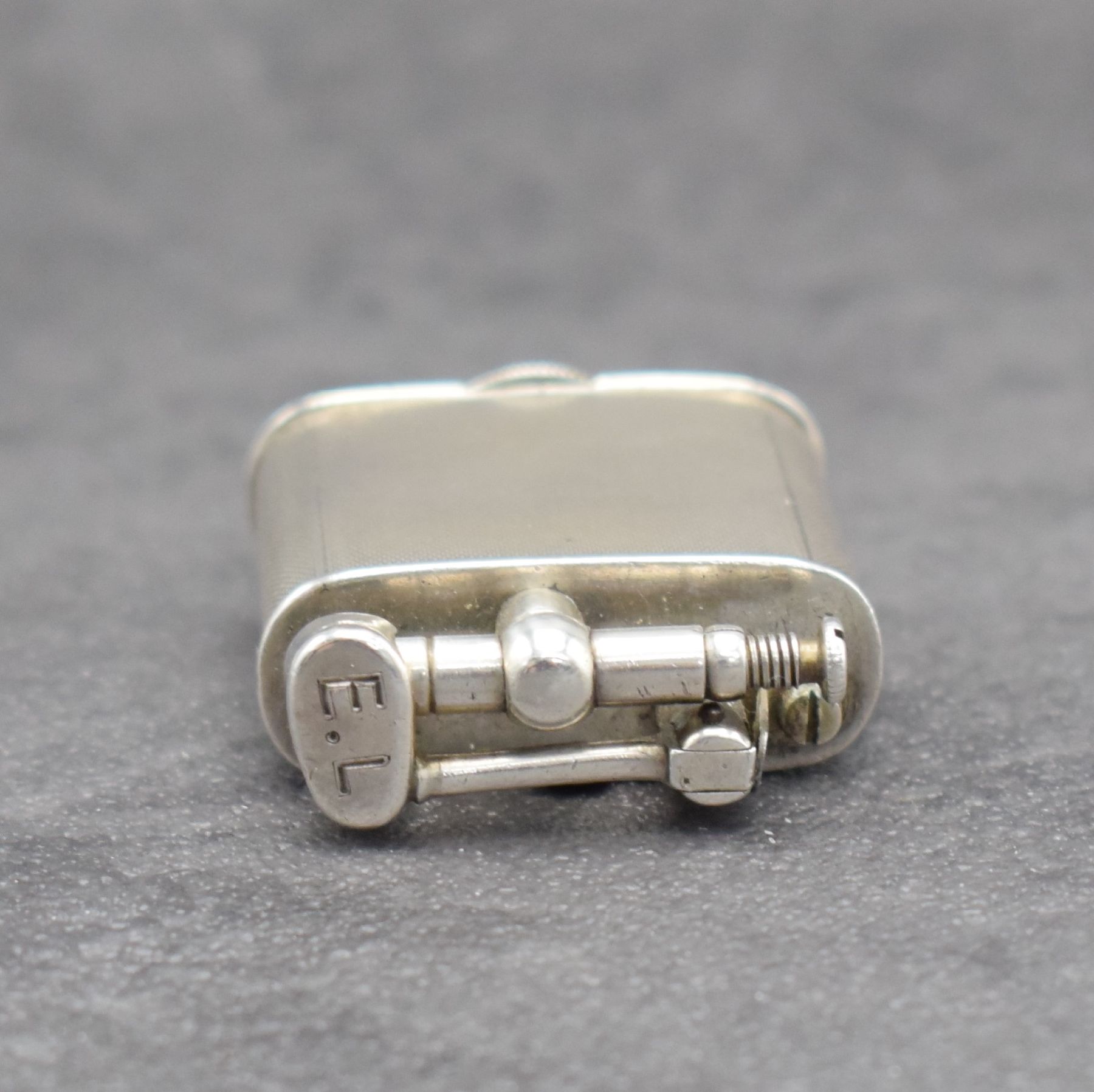 Detail e: Benzinfeuerzeug mit eingelassener Uhr in 900er Silber, Schweiz um 1930, rundum guill. Geh., Front mit Scharnier aufklappbar, Boden über verg. Werk ...