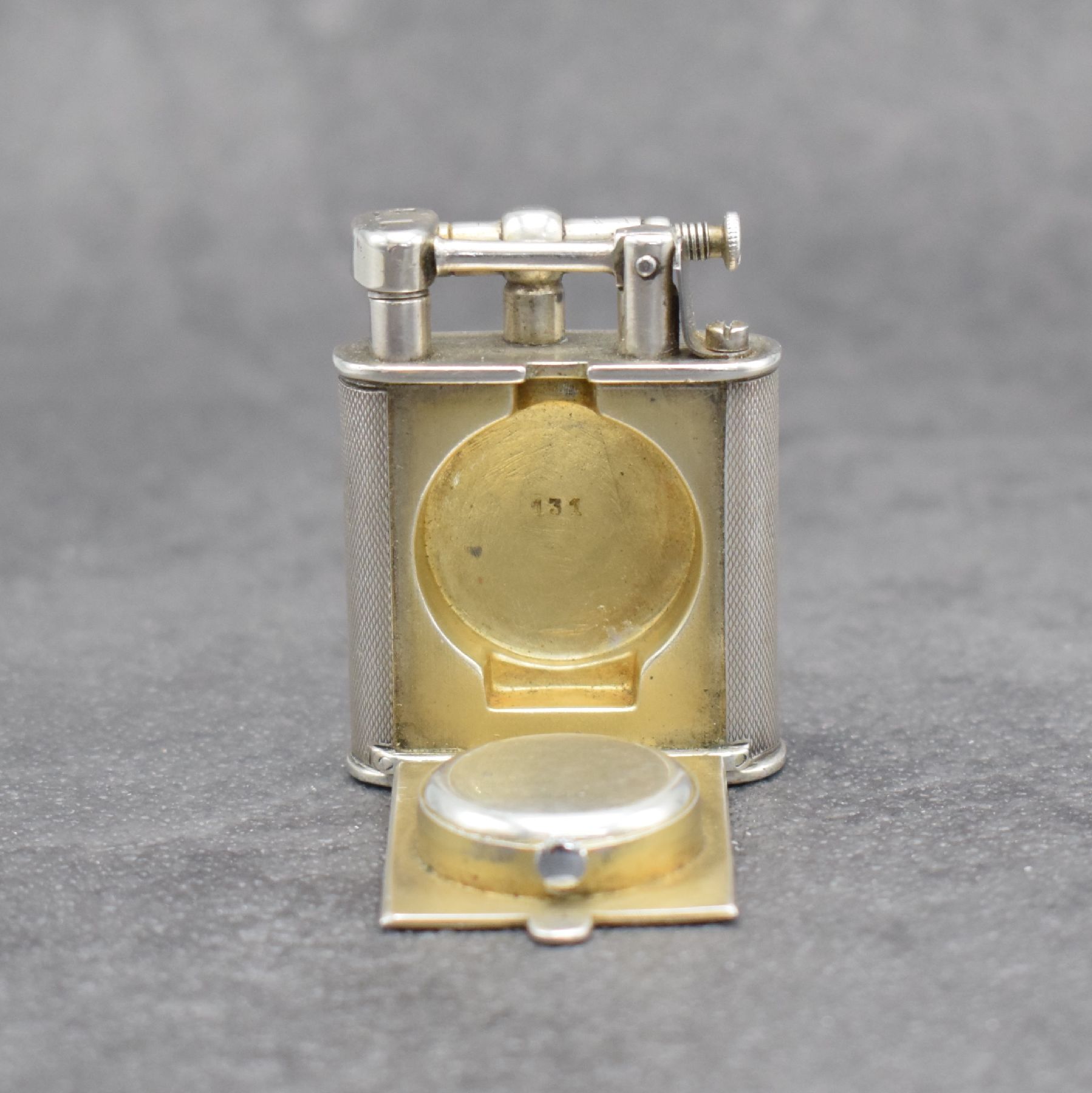 Detail g: Benzinfeuerzeug mit eingelassener Uhr in 900er Silber, Schweiz um 1930, rundum guill. Geh., Front mit Scharnier aufklappbar, Boden über verg. Werk ...