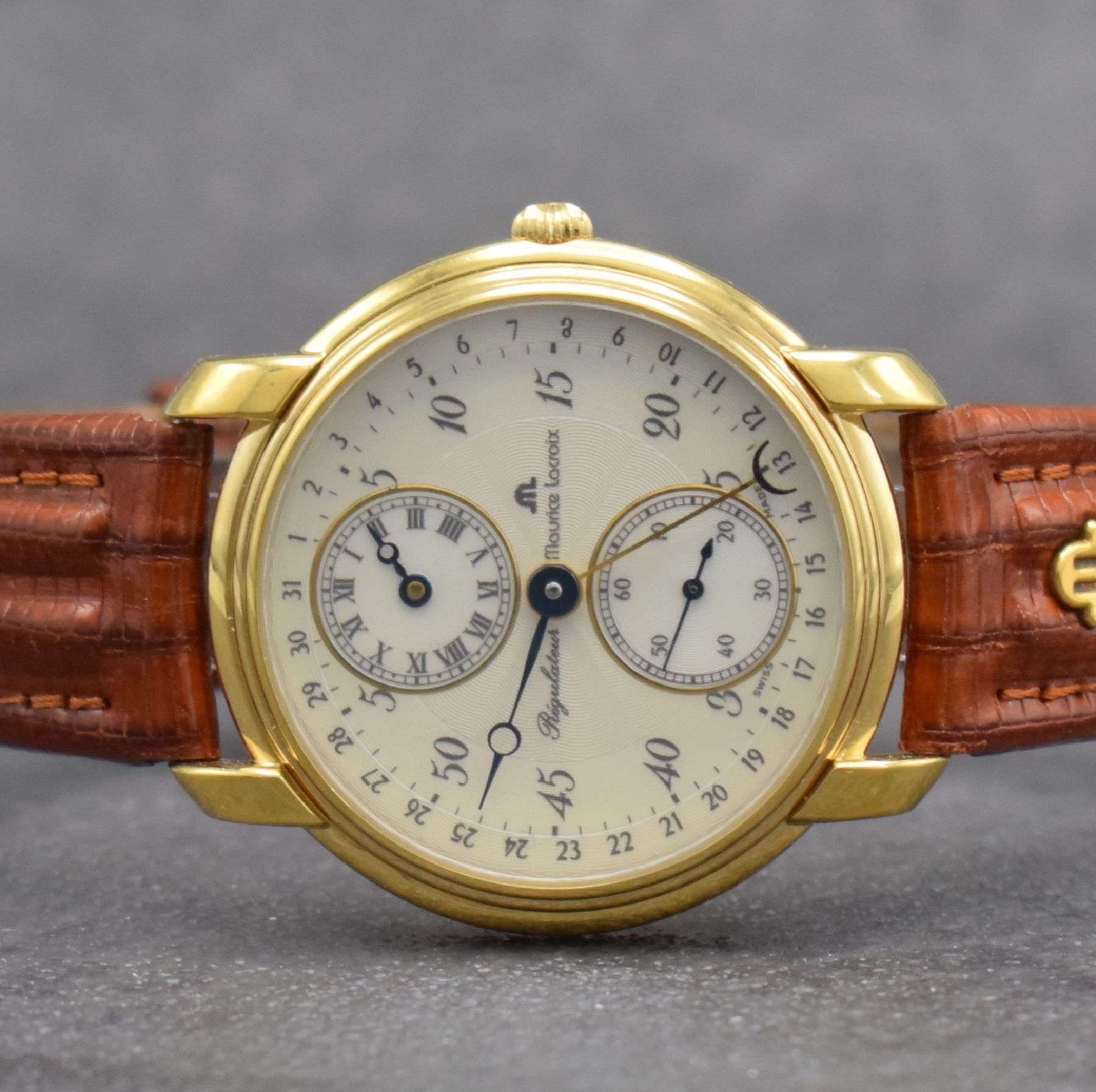 Detail a: MAURICE LACROIX Regulateur vergoldete Herrenarmbanduhr, Schweiz um 1990, Handaufzug, beids. vergl. Geh., Boden & Glasrand aufgedr., orig. Lederband ...